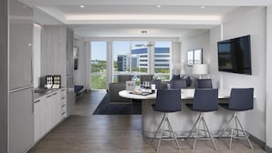 Une chambre d’hôtel moderne dotée d’une cuisine, d’un coin repas et d’une grande fenêtre donnant sur la ville.