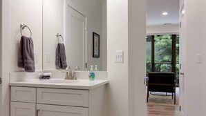 Un bagno moderno con uno specchio grande, mobili bianchi e un pavimento in legno chiaro.