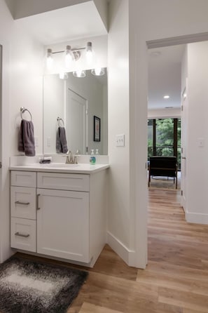 Enjoy a refreshing bathroom with a large mirror, vanity, and towels, plus a door leading to a balcony with a tree view.