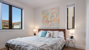 Camera da letto con un letto grande, due comodini, una finestra e un quadro astratto appeso al muro.