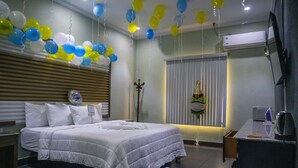A hotel room with a large bed, a bedside table, a TV, and a window with blinds. - Crown Hotel Piarco (Piarco)