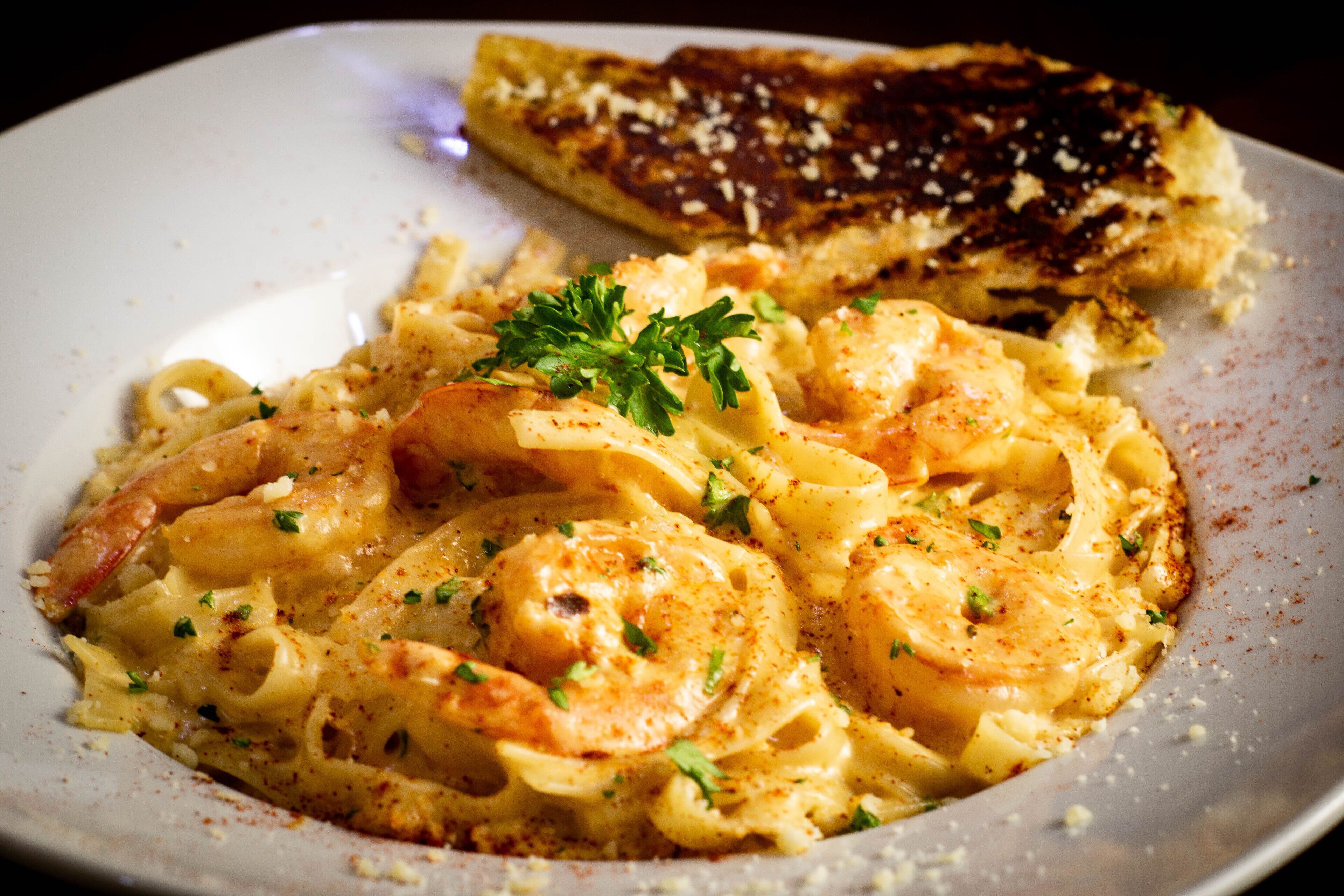 A plate of pasta with shrimp and a piece of grilled bread.