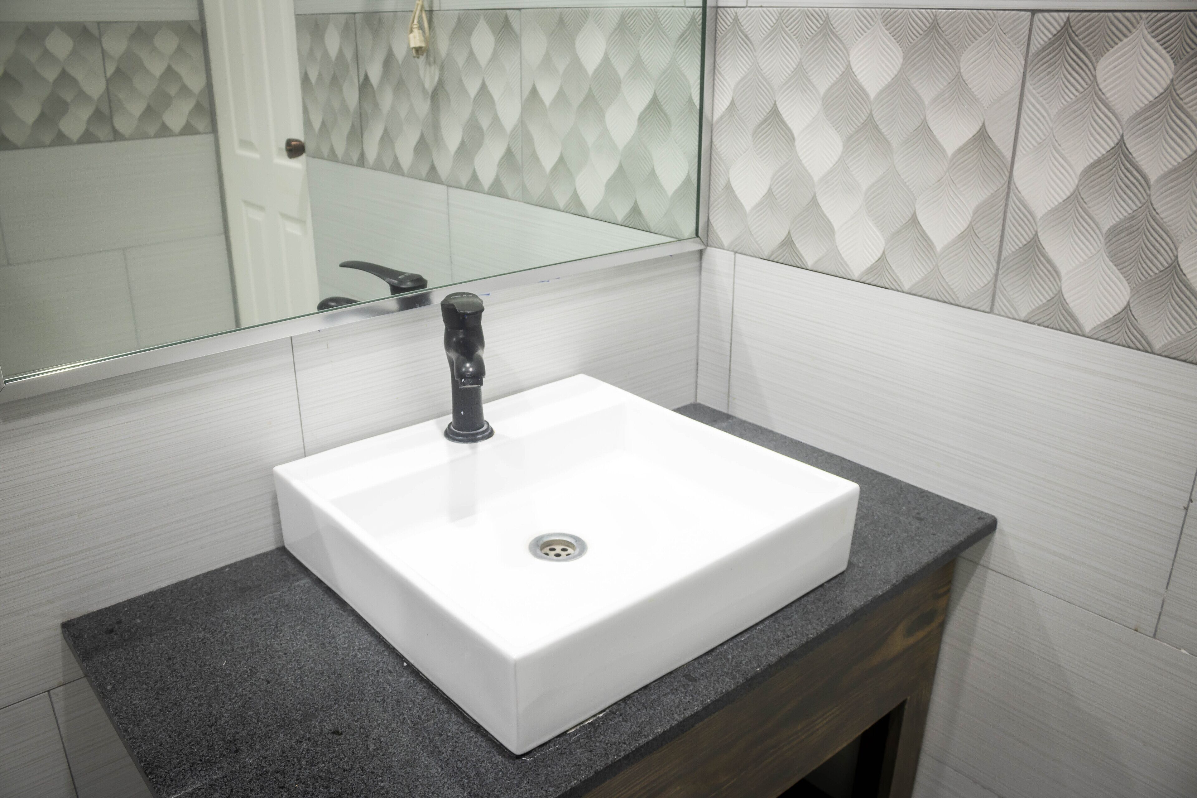 A bathroom with a white sink, dark countertop, and patterned wall tiles.