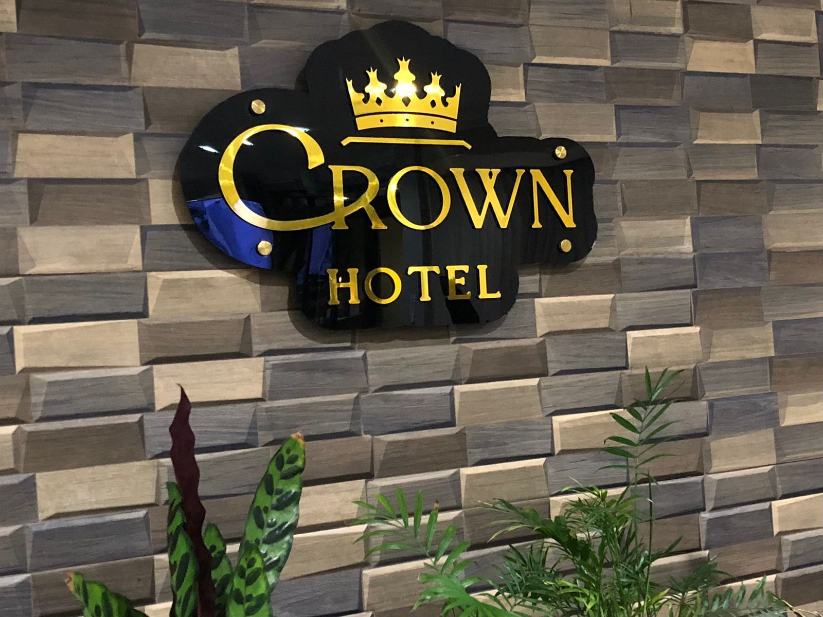 Letrero de hotel con logotipo de corona y el nombre 'Crown Hotel' en una pared con textura.