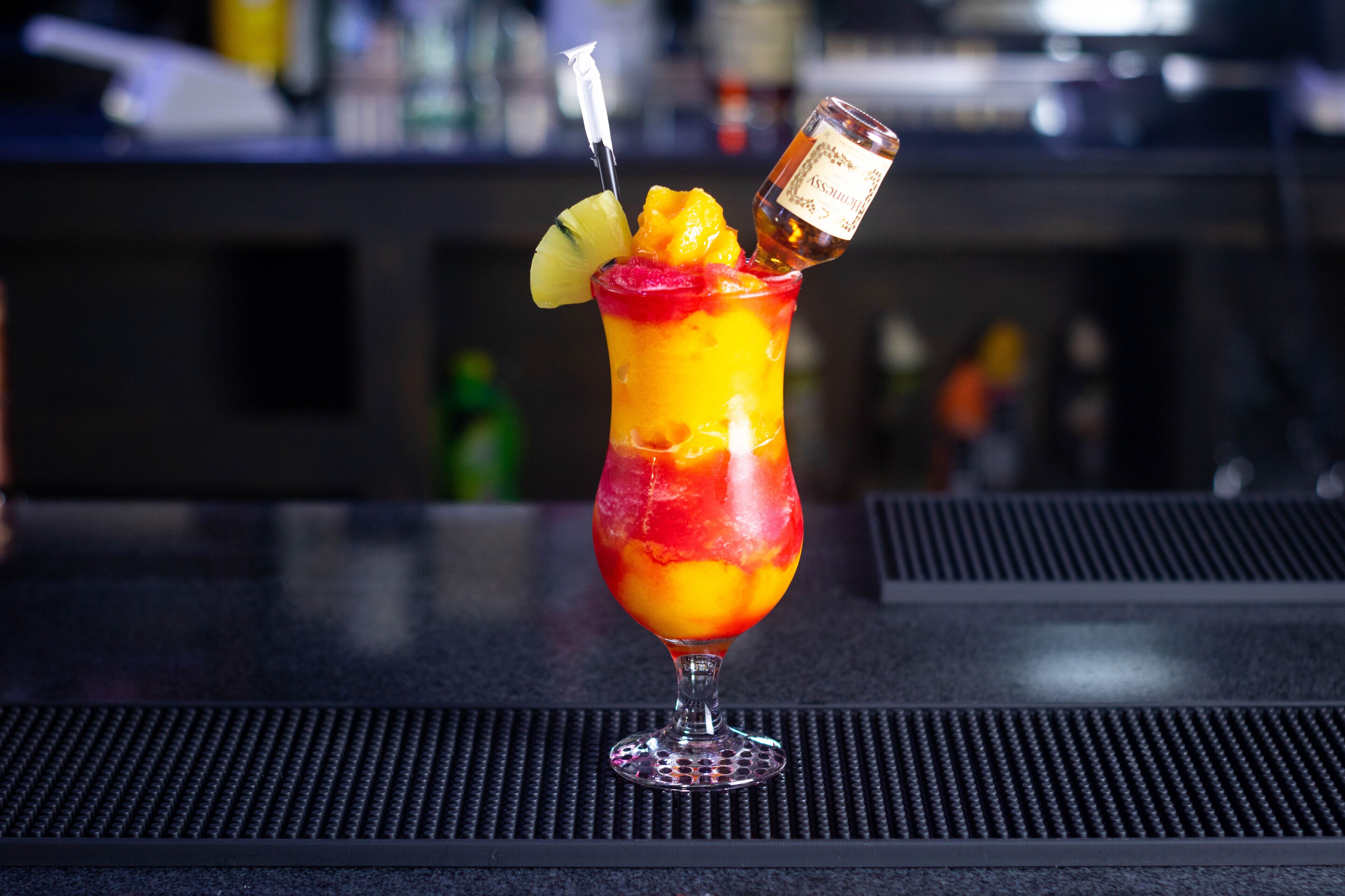 A cocktail in a glass with a straw and a bottle of liquor on the rim.