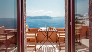 A balcony with a table, chairs, and a view of the sea and distant land. - Terracotta Cave House (2) (Santorini)