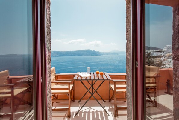 A balcony with a table, chairs, and a view of the sea and distant land. - Terracotta Cave House (2) (Santorini)