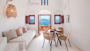 A room with a white sofa, wicker chairs, a dining table, and a view of the sea through an open archway. - Terracotta Cave House (2) (Santorini)
