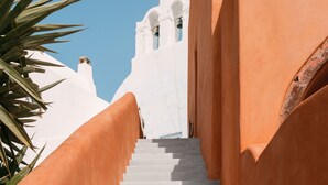 A staircase with white steps leading up to a white building with a bell tower. - Terracotta Cave House (2) (Santorini)