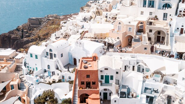A coastal village with white buildings, a rocky shoreline, and a view of the sea. - Terracotta Cave House (2) (Santorini)