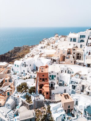 A coastal village with white buildings, a rocky shoreline, and a view of the sea. - Terracotta Cave House (2) (Santorini)