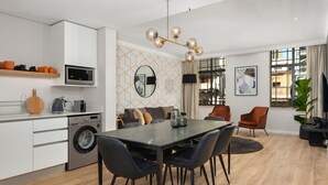 A modern kitchen with a microwave, washing machine, and a dining area with a table and chairs. - Modern and Sophisticated 2 Bedroom Apartment (Cape Town)