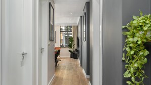 A hallway with a wooden floor, white walls, and a plant on the right. - Modern and Sophisticated 2 Bedroom Apartment (Cape Town)