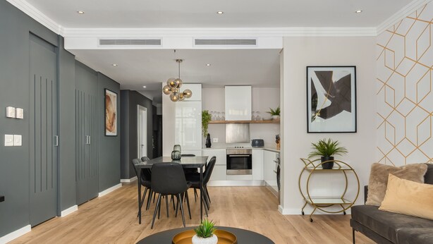A modern living room with a dining area, kitchen, and a grey wall with a geometric pattern. - Modern and Sophisticated 2 Bedroom Apartment (Cape Town)