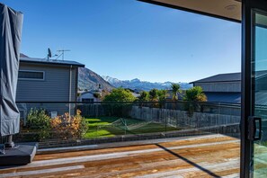 Ein modernes Haus mit Holzterrasse, einer Glastür, die auf einen Balkon führt, und Blick auf die Berge.