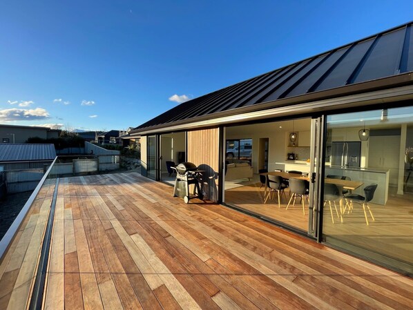 A modern house with a wooden deck, a barbecue, and a glass-enclosed dining area.