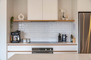 Una cocina moderna con armarios blancos, un refrigerador de acero inoxidable y una cafetera.
