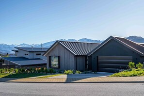 A modern two-story house with a garage, surrounded by a well-maintained lawn and a mountain backdrop.