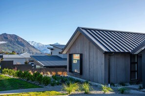 Una casa moderna con techo metálico inclinado, revestimiento de madera y camino de entrada de grava con jardines ajardinados.