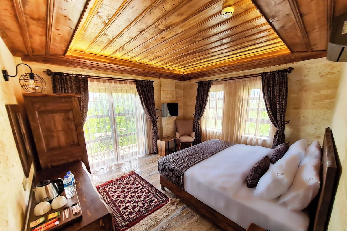 Een slaapkamer met houten lambrisering, een bed, gordijnen, een stoel, een bureau met toiletartikelen en uitzicht door grote ramen.