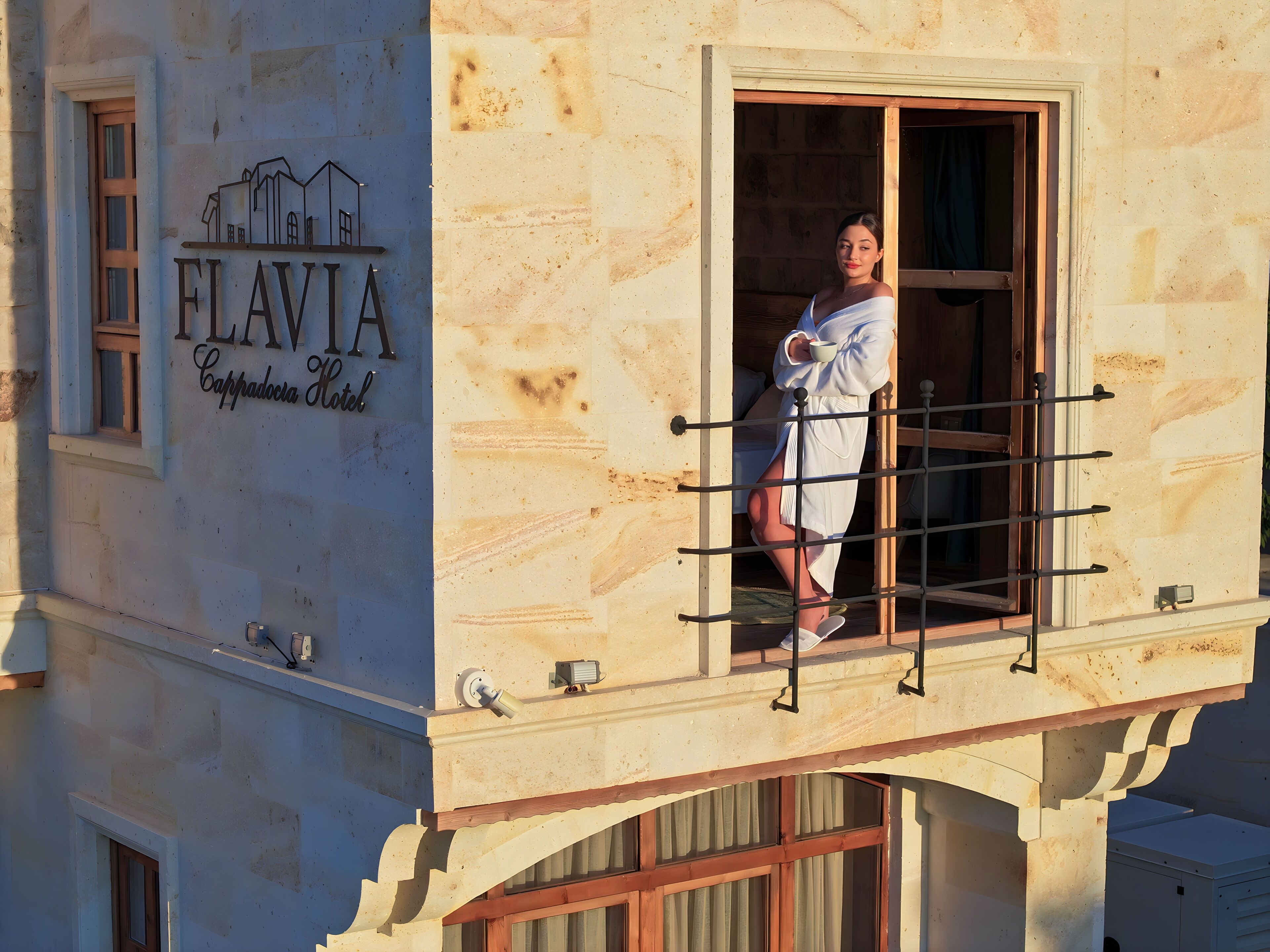 Un hotel chiamato FLAVIA con facciata in pietra, un balcone con ringhiera in metallo e una finestra con tende.
