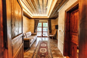 A hallway with a wooden ceiling, a sofa, a chair, a rug, and a door.