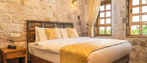 Un dormitorio con pared de piedra, estructura de cama de madera, mesita de noche y ventana con cortinas.
