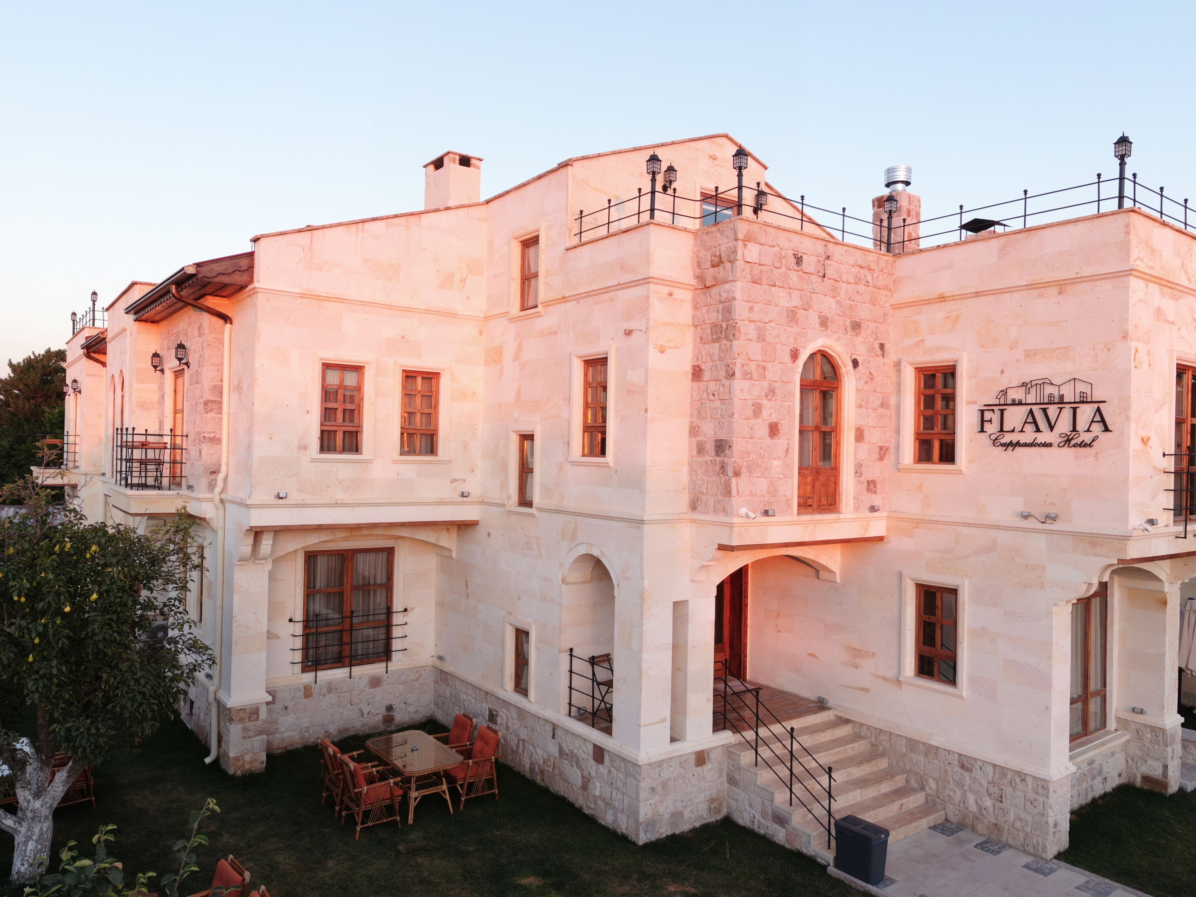A multi-story building with a stone facade, a sign reading 'FLAVIA Cappadocia Hotel,' and a courtyard with outdoor seating.
