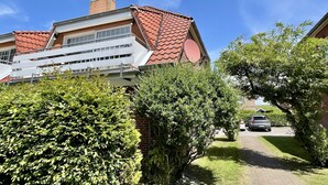 Een woongebouw met een rode dakbedekking, een wit balkon en een bakstenen schoorsteen.