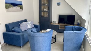 Een woonkamer met een blauwe bank, twee blauwe fauteuils, een televisie en een kast met glazen deuren.