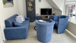 Een moderne woonkamer met een blauwe zithoek, een ronde salontafel en een televisie.
