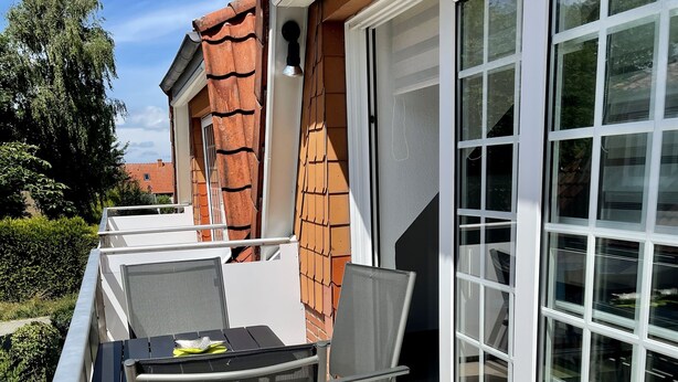 Een balkon met een tafel, stoelen, een schuifpui en een bakstenen muur.