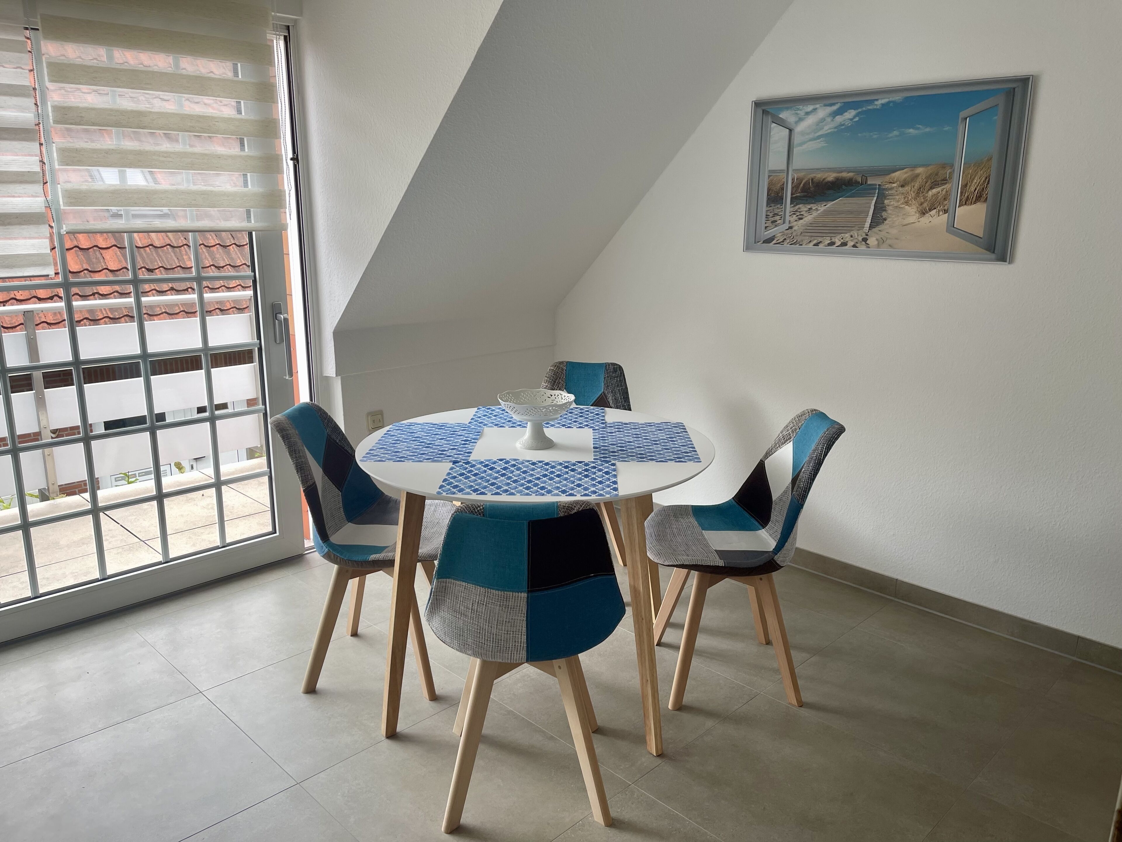 Ein Essbereich mit einem runden Tisch, vier Stühlen und einem Gemälde mit Strandmotiv an der Wand.