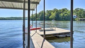 A dock with a covered seating area, a lifebuoy, and a small boat in the background. - Dock & Boat Slip! Waterfront Lake Ozark Home (Lake Ozark)