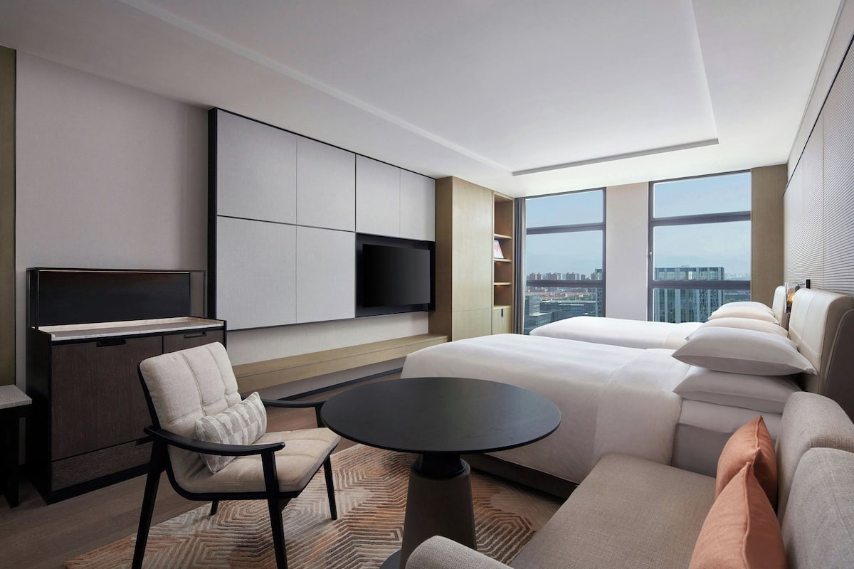 A modern hotel room with a large bed, a sofa, a small table, and a TV mounted on the wall.