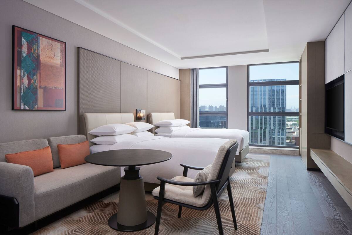 A modern hotel room with a large bed, a sofa, a dining table, and a TV.