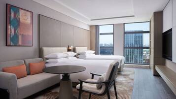 A modern hotel room with a large bed, a sofa, a dining table, and a TV.