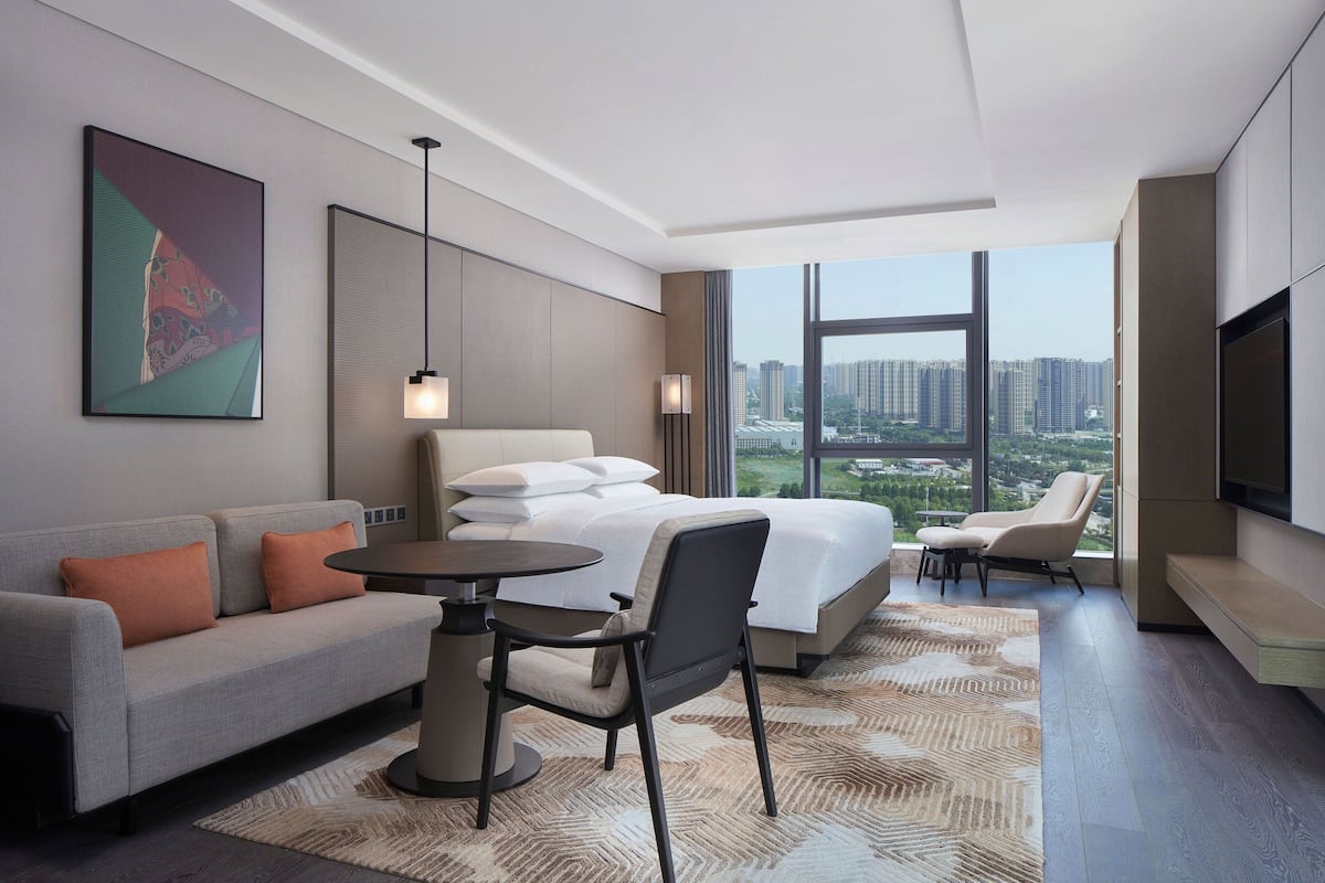 A modern hotel room with a large bed, a sofa, a dining table, and a TV.