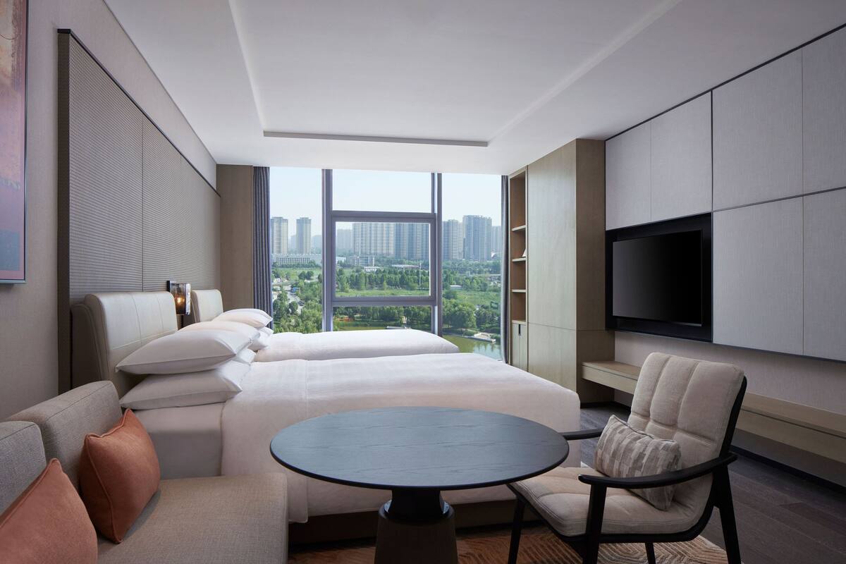 A modern hotel room with a large bed, a sofa, a round table, and a TV.