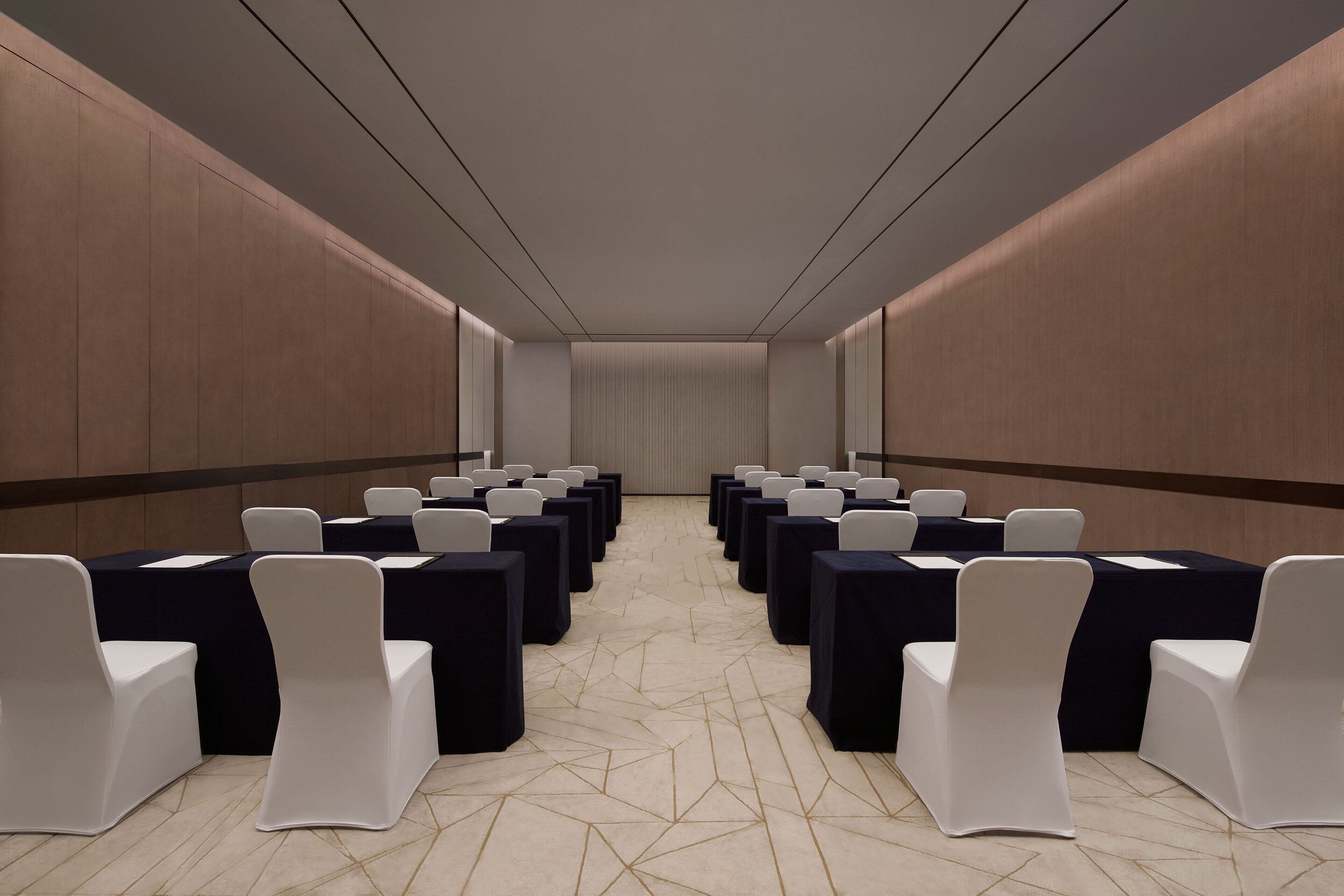 A conference room with rows of tables and chairs, a patterned carpet, and a neutral color scheme.