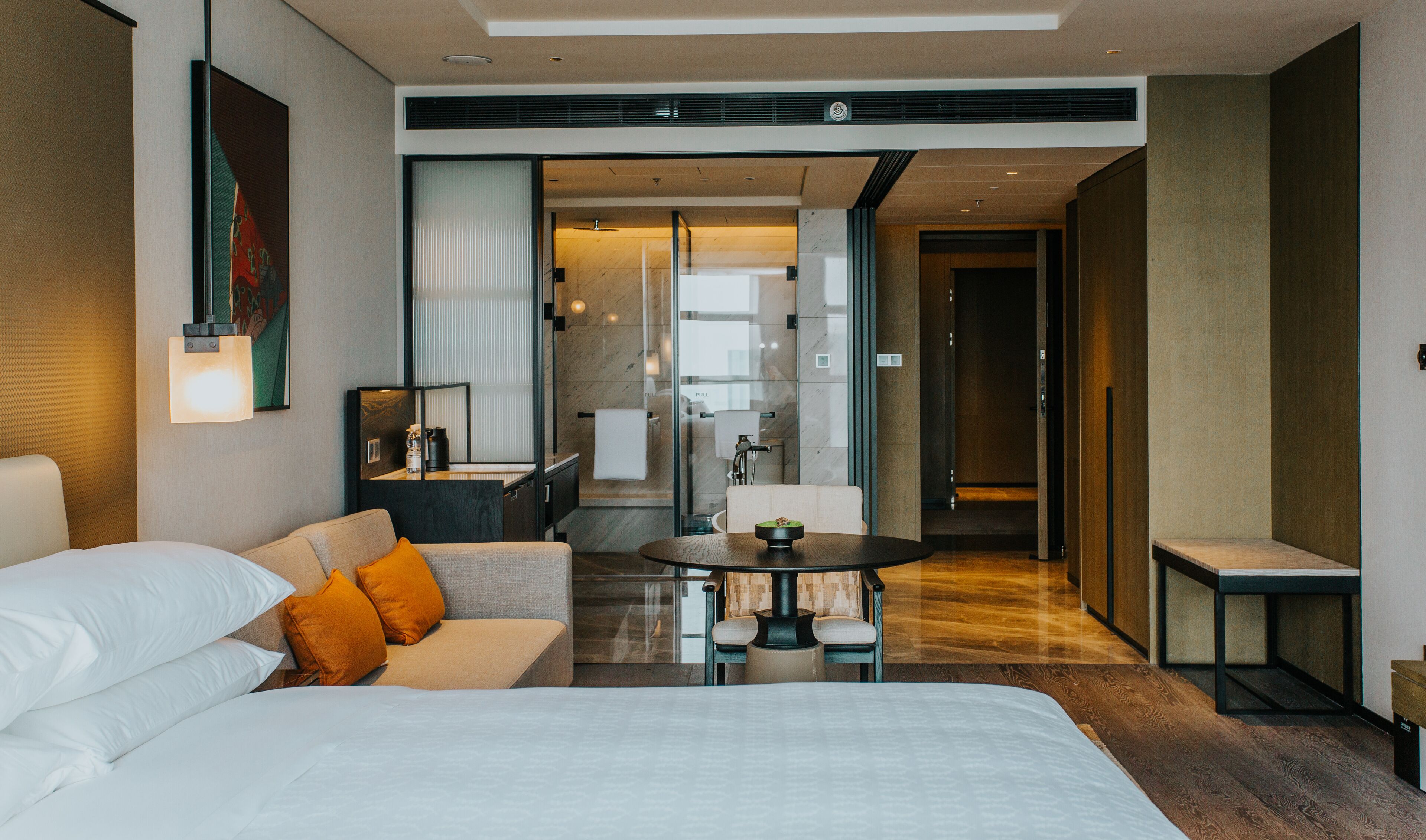 A modern hotel room with a large bed, a sofa, a small table, and a separate seating area.