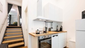 Een kleine keuken met een houten trap, witte kastjes en een inbouwoven.