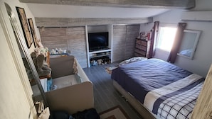 Een compacte slaapkamer met een bed, een televisie en een klein zithoekje.