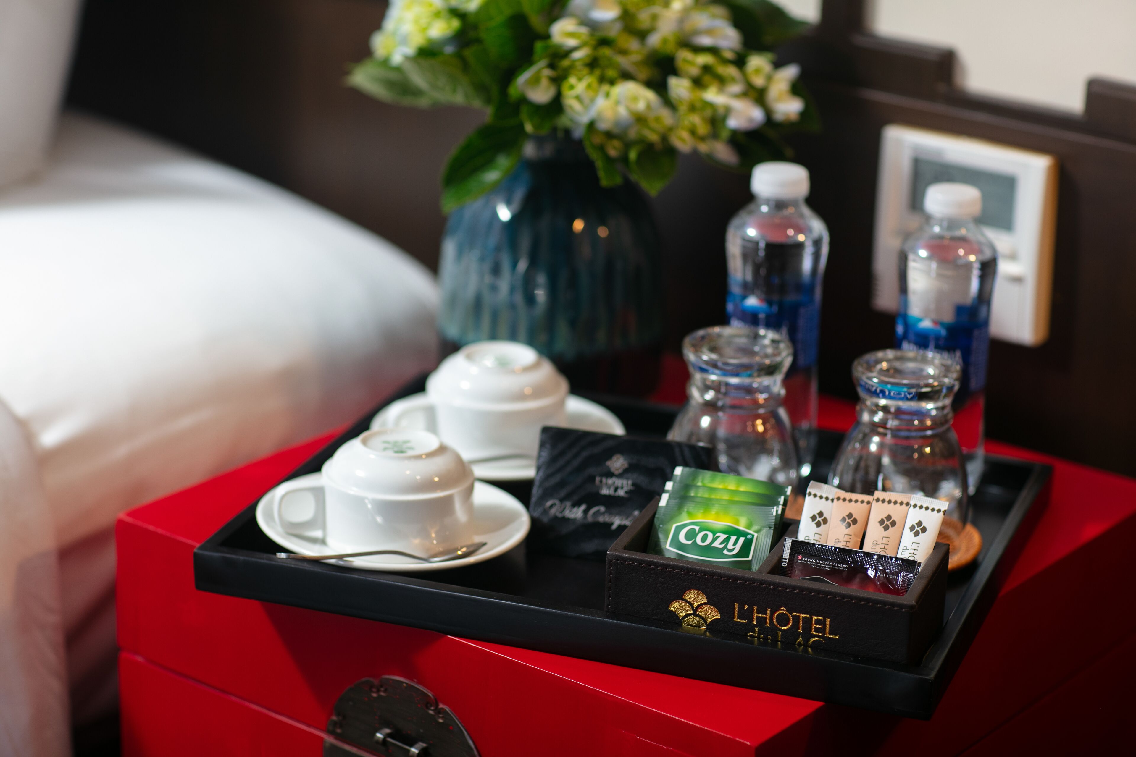 Bandeja de desayuno en una habitación de hotel con bolsitas de té, una botella de agua y un florero.