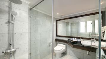 A modern bathroom with a glass-enclosed shower, a white toilet, and a large mirror above a sink.