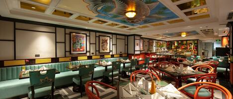 A restaurant with green booths and red chairs, featuring a ceiling mural of a dragon.