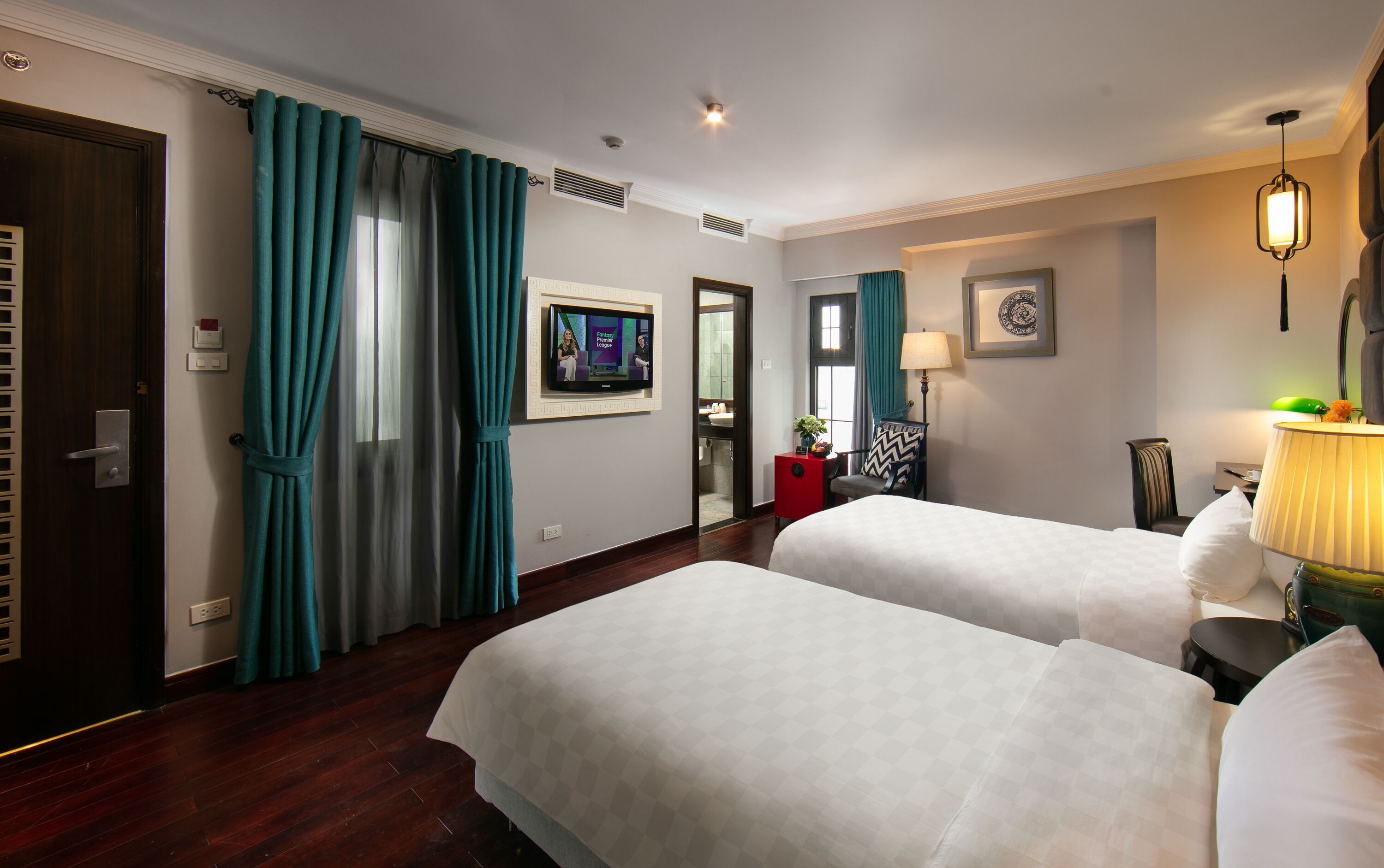 A hotel room with two beds, a TV, a desk, and a bathroom visible through an open door.