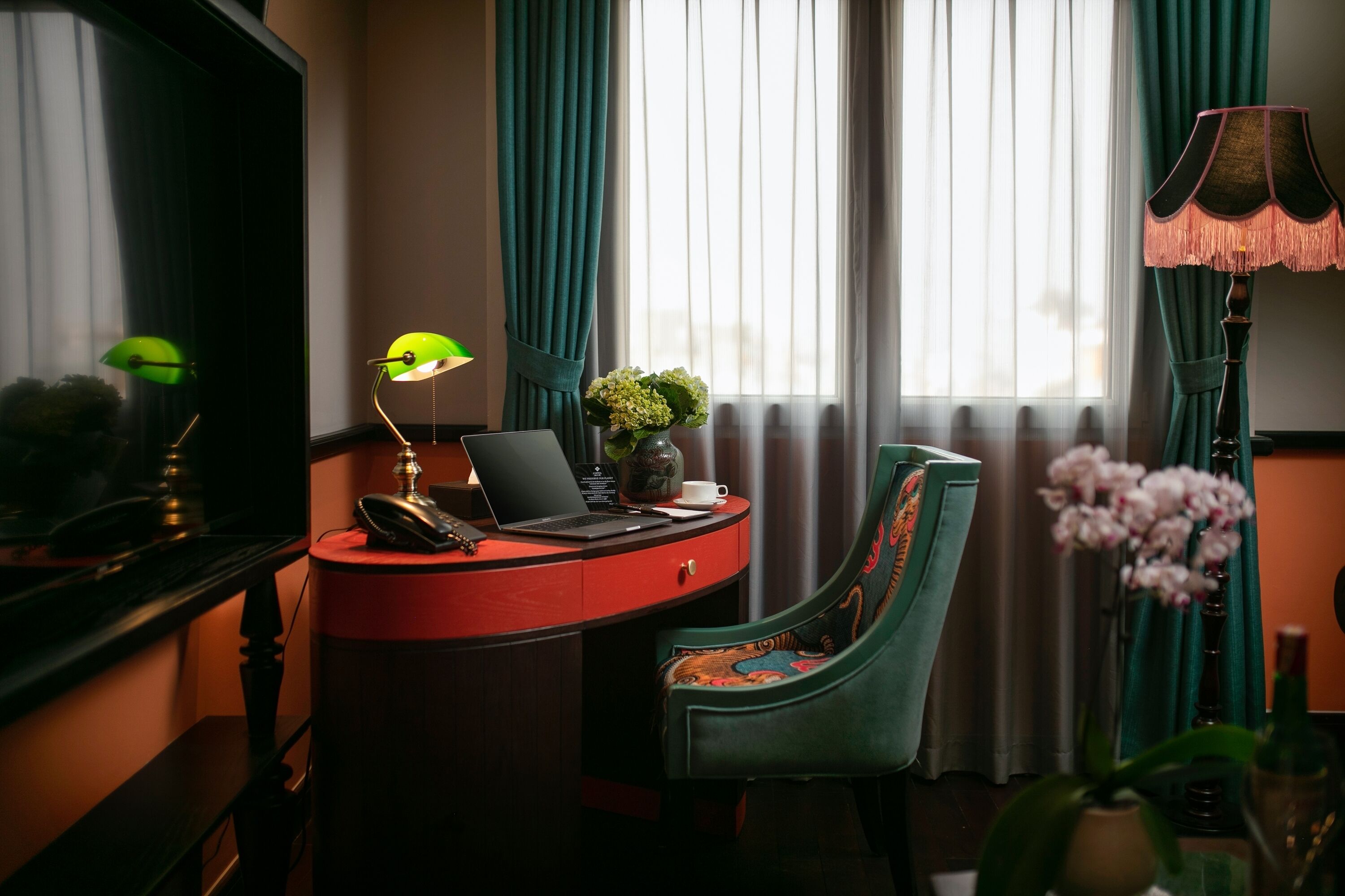 Une pièce comprenant un bureau, un ordinateur portable, une lampe, une chaise et une fenêtre avec des rideaux.