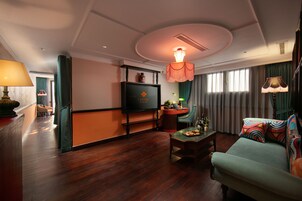 Una habitación de hotel con televisión, sofá, mesa de centro y mesa de comedor.