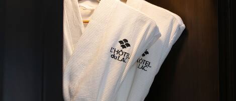 A white robe with "HOTEL du Lac" logo hanging on a wooden hanger.